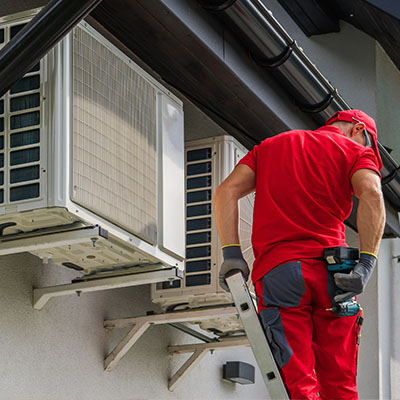 Asentaja punaisissa vaatteissa tikapuilla asentamassa ilmalämpöpumppua